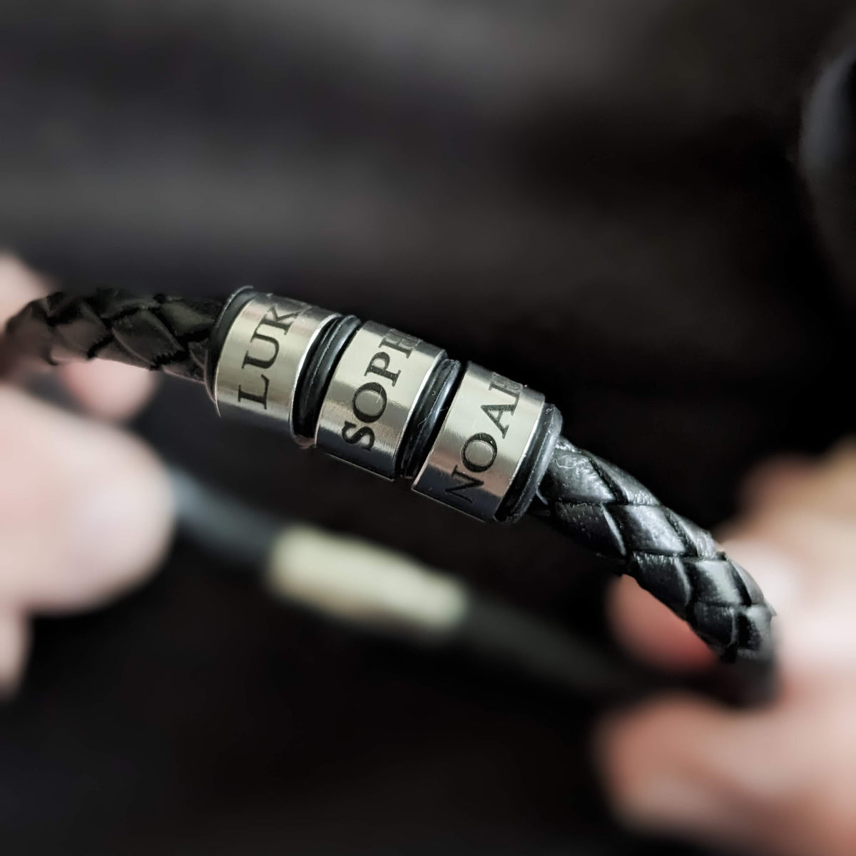 Close-up of black leather bracelet with personalised engraved stainless steel name rings