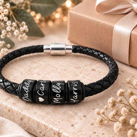 Black braided leather bracelet with four personalised black name rings, displayed with a gift box and dried flowers.